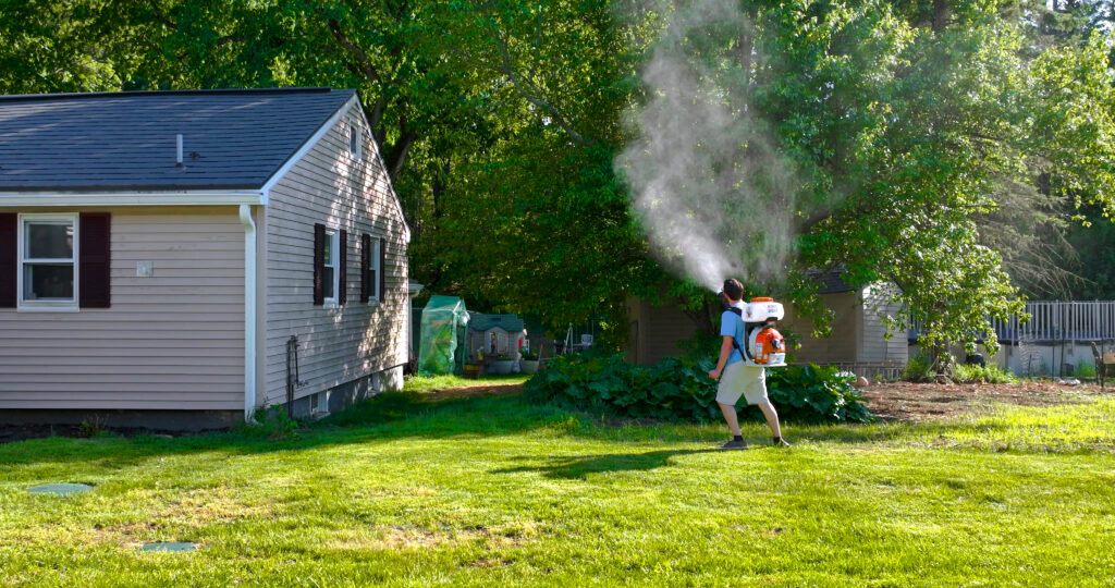Mosquito Enemy technician treating shaded shrubs near a backyard deck in Massachusetts.
